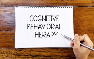 Cognitive behavioral therapy handwriting text on blank notebook paper on wooden table with hand holding pencil. Business concept and legal concept about Cognitive behavioral therapy.